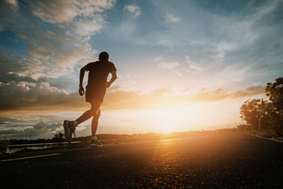 man running on the side of road at sunset 
